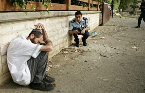 A policeman and a paramedic, left, take cover as rockets fired from the Gaza Strip hit Sderot, Sunday. (AP)
